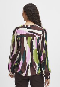 Mehrfarbige Bluse mit lebhaften abstrakten Mustern in Pink, Grün, Braun und Schwarz. Lange Ärmel mit gerafften Manschetten und Rüschenausschnitt.