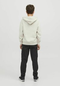Felpa con cappuccio beige e pantaloni cargo neri. Tessuto morbido, vestibilità rilassata, polsini a costine e molteplici tasche sui pantaloni. Sneakers nere.