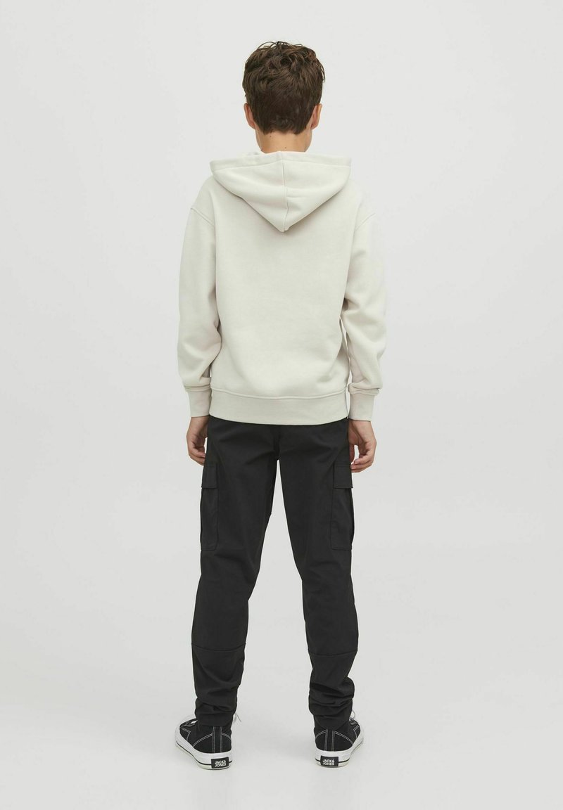 Sweat-shirt à capuche beige et pantalon cargo noir. Tissu doux, coupe décontractée, poignets côtelés et plusieurs poches sur le pantalon. Baskets noires.