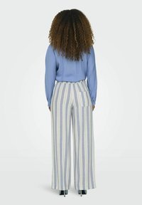 Lichtblauwe blouse met lange mouwen, gecombineerd met wijde broekspijpen met verticale lichte en donkere strepen en een achterzak.