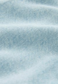 Světlá modrá džínovina s viditelnou diagonální texturou tkaní a měkkými záhyby.