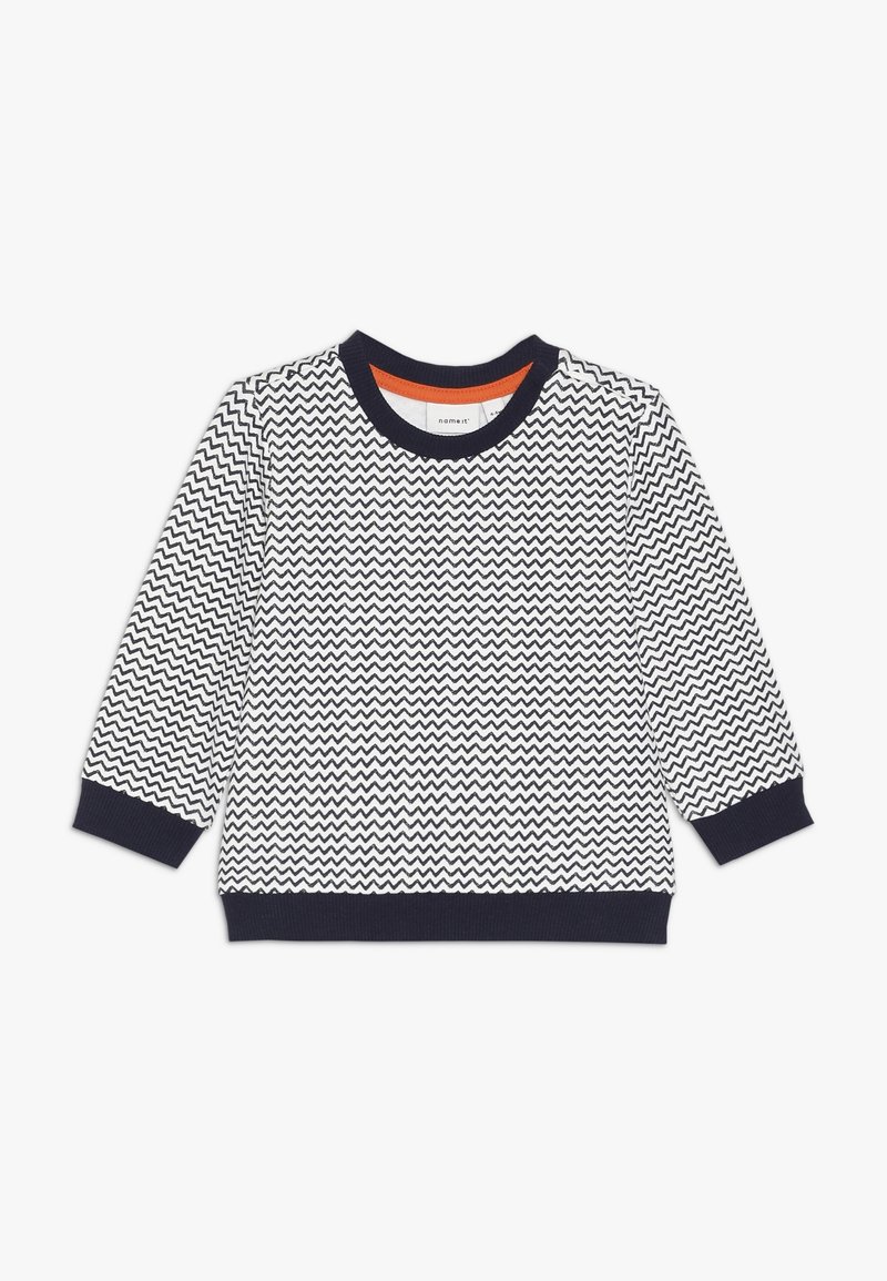 Pull en zigzag bleu marine et blanc avec des manches longues et des poignets côtelés. Présente un col intérieur orange contrastant. Fabriqué en tissu doux.