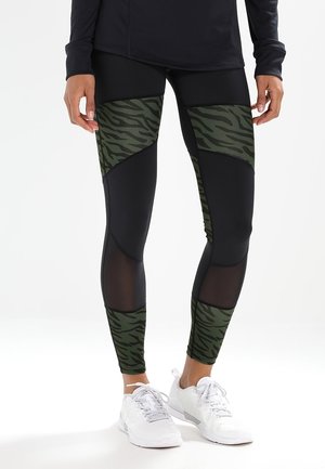 Black leggings featuring green tiger stripe panels, mesh accents, and a fitted design. Worn with white athletic shoes.