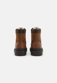 Botas de tobillo de cuero marrón con un acabado texturizado, un acento en marrón más oscuro en el cuello y una suela de goma negra. Cierre con cremallera en el lateral.