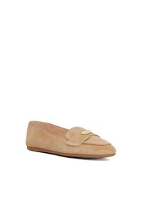 Beige suède instappers met een ronde neus, voorzien van een goudkleurig logoaccent op de wreef en een platte rubberen zool. Gladde textuur.
