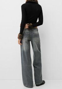 Svart ribbad långärmad topp med leopardmönstrade fuskpälsfållar, i kombination med ljusgrå vida jeans med viss blekning och bakfickor.