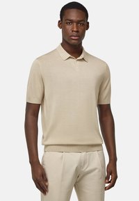 Krémové polo tričko s krátkým rukávem vyrobené z jemného pleteného materiálu. Má klasický límeček a zapínání na tři knoflíky. Hladká textura, štíhlý střih.