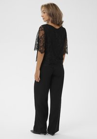 Top in pizzo nero con maniche a lunghezza gomito abbinato a pantaloni larghi neri. Il top presenta intricati motivi floreali e una vestibilità comoda.