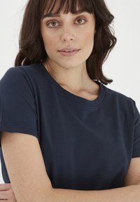 Tricou din bumbac de culoare albastru marin, cu guler rotund și mâneci scurte, având o textură netedă și detalii de cusătură minime.