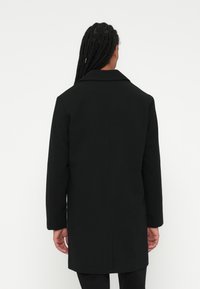 Svart ullblanding overcoat med spiss krage, rett snitt og lange ermer, med en glatt tekstur og detaljert bak søm.