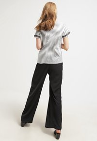 Camiseta de rayas grises y blancas de manga corta, combinada con pantalones anchos negros, vista por detrás. Tejido suave, diseño sencillo.