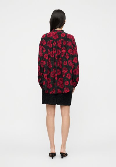 Λουλουδάτο μπλουζάκι με κόκκινο σχέδιο τριαντάφυλλου σε μαύρο φόντο, μακριά μανίκια και άνετη εφαρμογή. Συνδυασμένο με μαύρη δαντελένια φούστα.