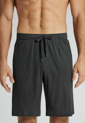 Mannelijke torso met zwarte knielange shorts met een elastische tailleband en trekkoord, handen ontspannen langs de zijkanten.