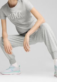 T-shirt in cotone grigio con logo "PUMA", abbinato a pantaloni da jogging coordinati e sneakers azzurre chiare con accenti rosa e dettagli menta.