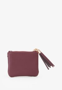 Portamonete in pelle bordeaux con cerniera dorata e dettaglio decorativo a frangia sul cursore della cerniera. Texture liscia, design compatto.