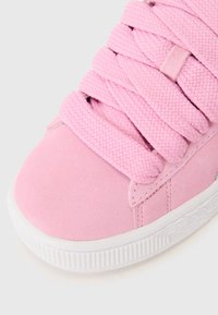 Sneaker in suede rosa con lacci spessi intrecciati, punta rotonda e suola in gomma bianca con dettagli testurizzati lungo il bordo inferiore.
