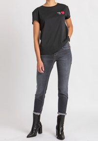 Camiseta negra de manga corta con un gráfico de un corazón rojo, combinada con jeans de mezclilla oscura y botas negras de tobillo con tacón alto.