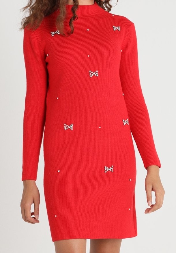 Femme portant une robe en maille rouge à manches longues avec un petit nœud décoratif et des ornements en perles.