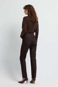 Jeans de tiro alto de color marrón oscuro con tejido texturizado, bolsillos traseros y un parche marrón claro en la cintura, combinados con una blusa marrón ajustada y tacones burdeos.