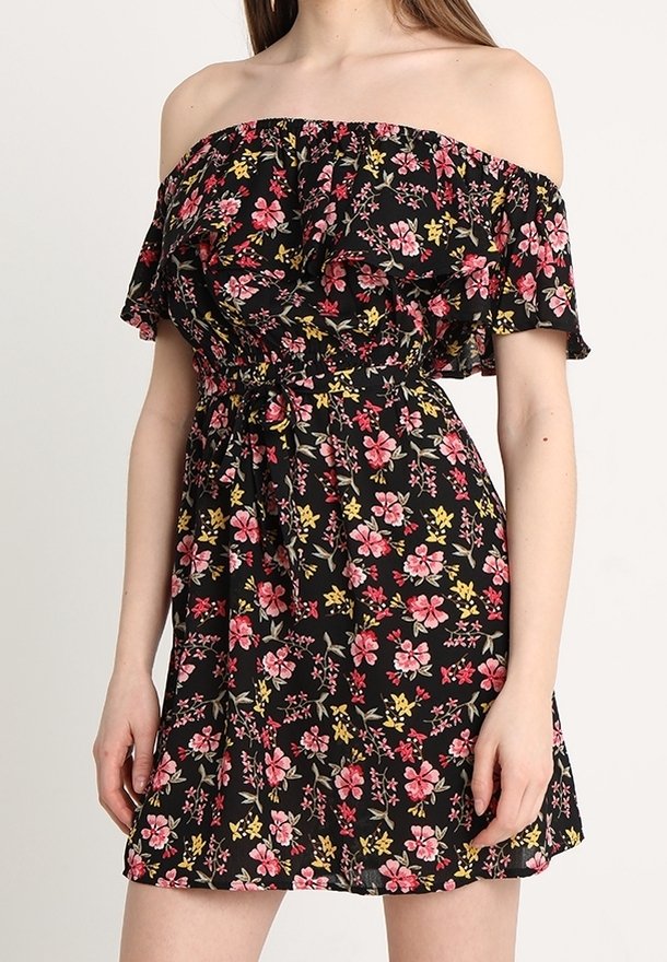 Femme portant une robe noire épaules dénudées avec des motifs floraux roses, rouges et jaunes et un col à volants.