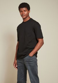 T-shirt nera di cotone con scollatura tonda e maniche corte, abbinata a jeans in denim grigio scuro. Il tessuto appare liscio con una vestibilità classica.