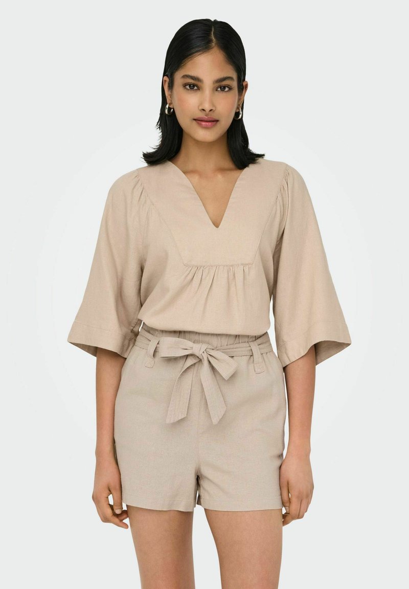 Beige Leinenoberteil mit V-Ausschnitt und kurzen Glockenärmeln, kombiniert mit passenden Hochbundshorts, die eine taillierte Akzentuierung aufweisen.