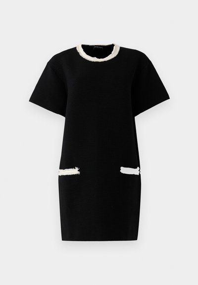 Black short-sleeve dress with textured fabric, white fringed neckline, and white fringed accents on front pockets.