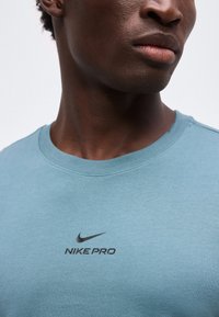 Κοντινό πλάνο ενός ατόμου που φοράει μπλούζα Nike Pro ανοιχτού μπλε χρώματος, δείχνοντας τον λαιμό και το λογότυπο στο στήθος.