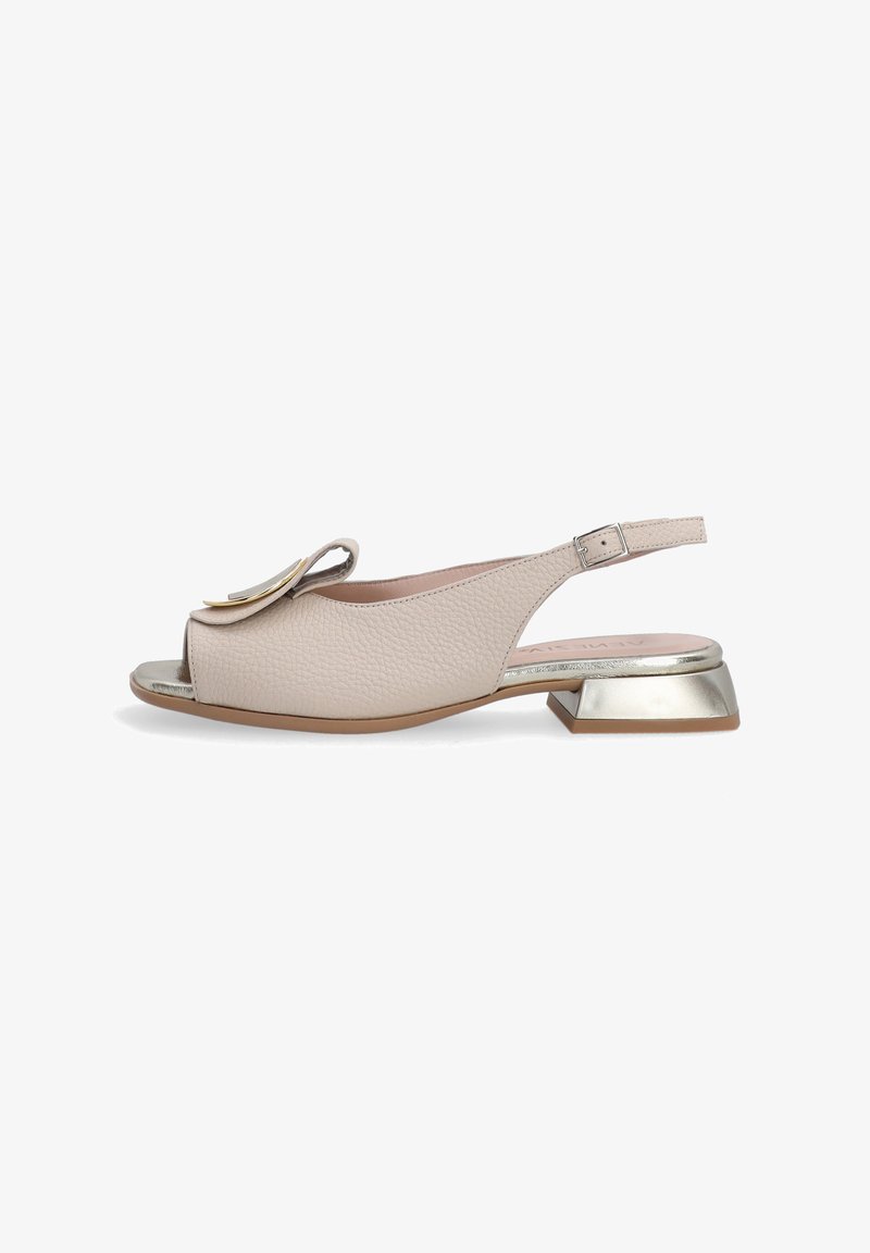 Beige leather slingback sandal with open toe, featuring a layered floral accent and a metallic block heel. Textured surface and adjustable strap.