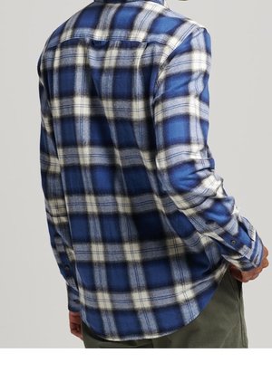 Camisa de franela a cuadros azul y blanco con mangas largas, dobladillo redondeado y puños abotonados. Textura suave y ajuste casual.