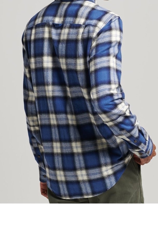 Camicia in flanella a quadri blu e bianchi con maniche lunghe, orlo arrotondato e polsini con bottoni. Texture morbida e vestibilità casual.