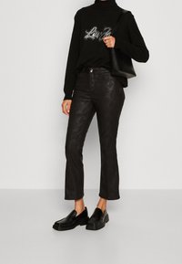 Svart polotröja med rhinestone-detaljer, i kombination med svarta mönstrade byxor och kraftiga svarta loafers. Väskan är svart med krokodilprägling.