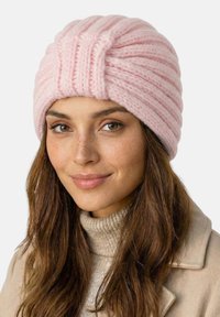 Lyserød strikket hue med ribbet design, der har en blød tekstur og en snoet top. Båret af en model med brunt hår, neutral baggrund.