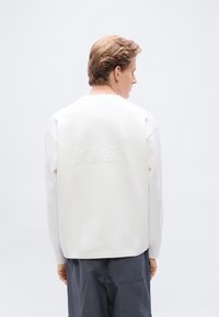 Λευκό φούτερ με στρογγυλή λαιμόκοψη και υφασμάτινο λογότυπο στην πλάτη, σε συνδυασμό με σκούρο μπλε σορτς. Το ύφασμα φαίνεται λείο και απαλό.