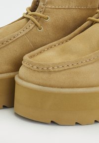 Brūni zamšādas potītes zābaki ar izšuvumu, apaļu purngalu un biezu platformas zoli. Iekļauti zeltaini acu caurumi un atbilstošas auklas.