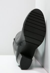 Botte en cuir noir avec une semelle en caoutchouc plate. Dispose d'une surface antidérapante texturée et d'une fermeture éclair extérieure décorative sur le côté.