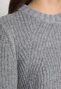 Szary dzianinowy sweter z teksturowanym wzorem z pionowymi żebrowaniami. Dekolt jest okrągły, a tkanina wydaje się miękka i ciepła.