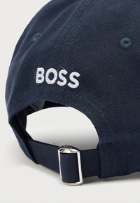 Granatowa czapka z bawełny z regulowanym paskiem. Posiada biały haftowany napis "BOSS" na tylnej części oraz fakturowaną tkaninę.