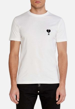 T-shirt bianca in cotone con scollatura rotonda, maniche corte e un design di cuore nero con linea spezzata e testo "JR" sul petto.