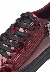 Sneaker in pelle verniciata rossa con lacci neri, dettaglio della cerniera laterale e finitura testurizzata. Punta arrotondata e suola in gomma nera.
