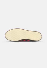 Sort sneakersål med en honningkagestruktur; med røde striber, en beige gummisål og en afrundet form.