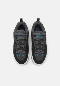 Ett par svarta Adidas-sneakers med grå snören och blå logotypdetaljer, sedd uppifrån mot en vit bakgrund.