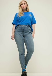 Camiseta de algodón azul con cuello redondo y mangas cortas, combinada con pantalones vaqueros ajustados de cintura alta en un tono azul claro.