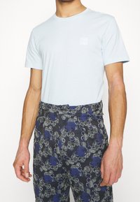 T-shirt en coton bleu clair avec un col ras du cou. Associé à un pantalon sombre à motifs avec des dessins floraux bleus, verts et gris et une fermeture à boutons.