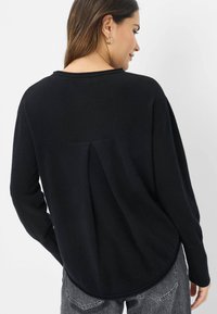 Schwarzer Strickpullover mit abgerundetem Saum, lässiger Passform und Schulternahtdetails. Lange Ärmel und weiche Textur. Einfaches, unaufdringliches Design.