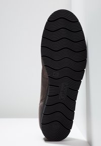 Semelle en caoutchouc noir avec un motif de bande de roulement ondulé sur une chaussure en daim marron, indiquant la taille 4½ et la marque "Gabor".