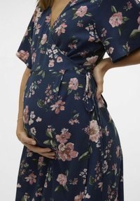 Robe portefeuille florale en bleu marine avec des fleurs roses. Manches courtes, décolleté en V et lien à la taille. Tissu texturé avec des accents verts terre.