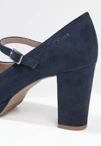 Talons en suède bleu marine avec un bout arrondi, une bride de cheville ajustable et un talon en bloc. Logo de la marque embossé sur le côté.