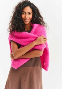 Puszysta, jaskraworóżowa szal owinięty wokół ramion, w połączeniu z brązowym topem. Miękka tekstura, otwarty fason i żywy kolor tworzą przytulny wygląd.