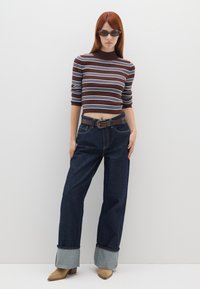 Braun und blau gestreifter, taillierter Rippstrickpullover kombiniert mit dunklen, weit geschnittenen Jeans mit umgeschlagenen Säumen und einem braunen Gürtel.